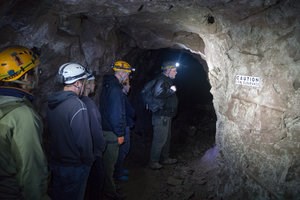 Adventure Mine Tour A group of people with hardhats and head lamps explore a former underground copper mine with a tour guide.