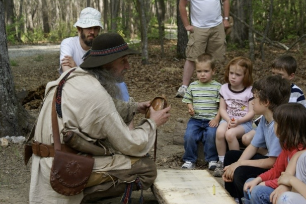 A park volunteer dressed in period costume addresses a group a children.