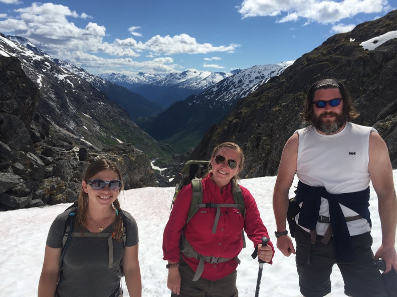 Three people stand on a mountain snow patch Three people stand on a mountain snow patch