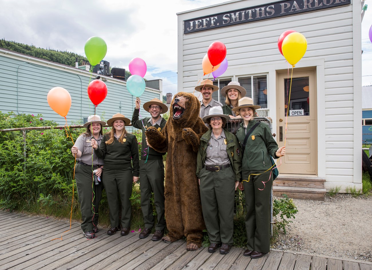 A group of rangers with balloons and a bear costume pose in front of the Jeff. Smiths Parlor.