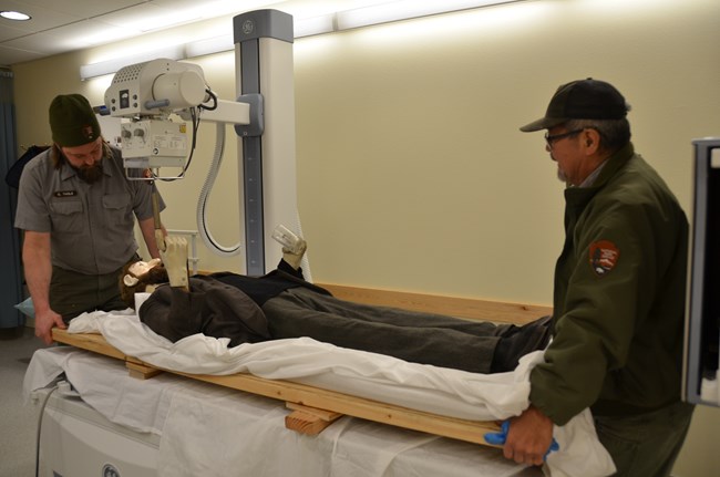 Maintenance staff load the Soapy Smith manikin onto a table to be X-rayed.
