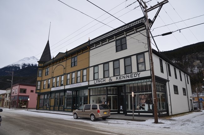 Snow dusted asphalt road in front of white wooden building with dark green trim