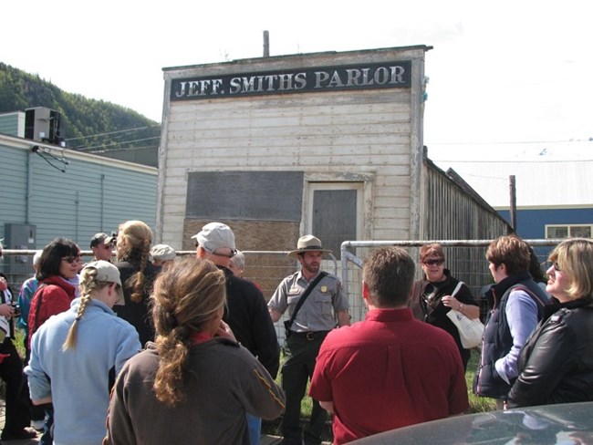 People gathered around a ranger in front of an old building.