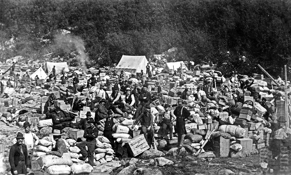 People sit among piles of bags and boxes and tents