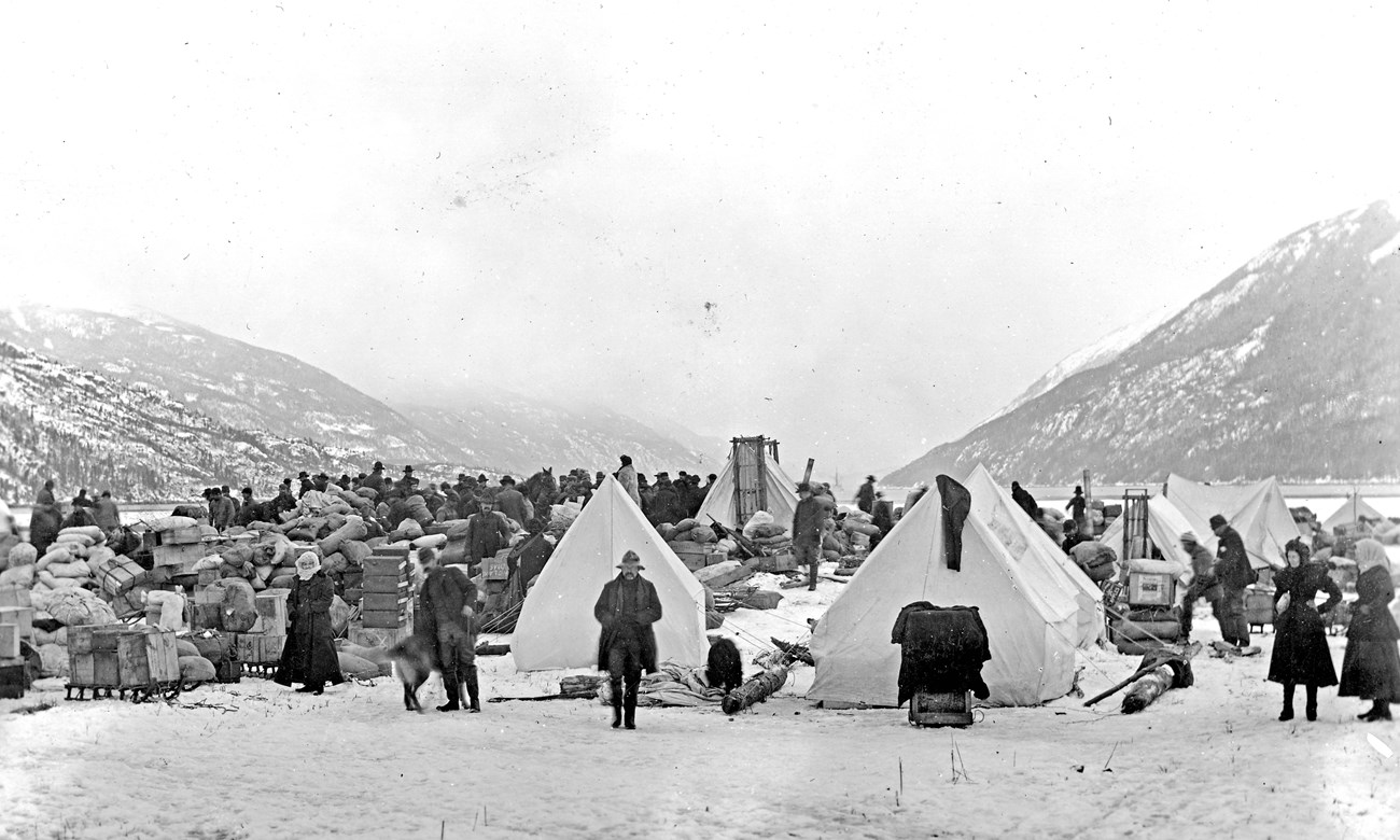 Black and white photo of tents, supplies, and people on a snowy beach