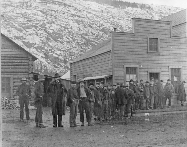 Men stand in a line in front of a wooden building in winter