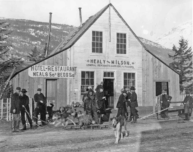 People stand in front of a wooden building with sign "Healy & Wilson"
