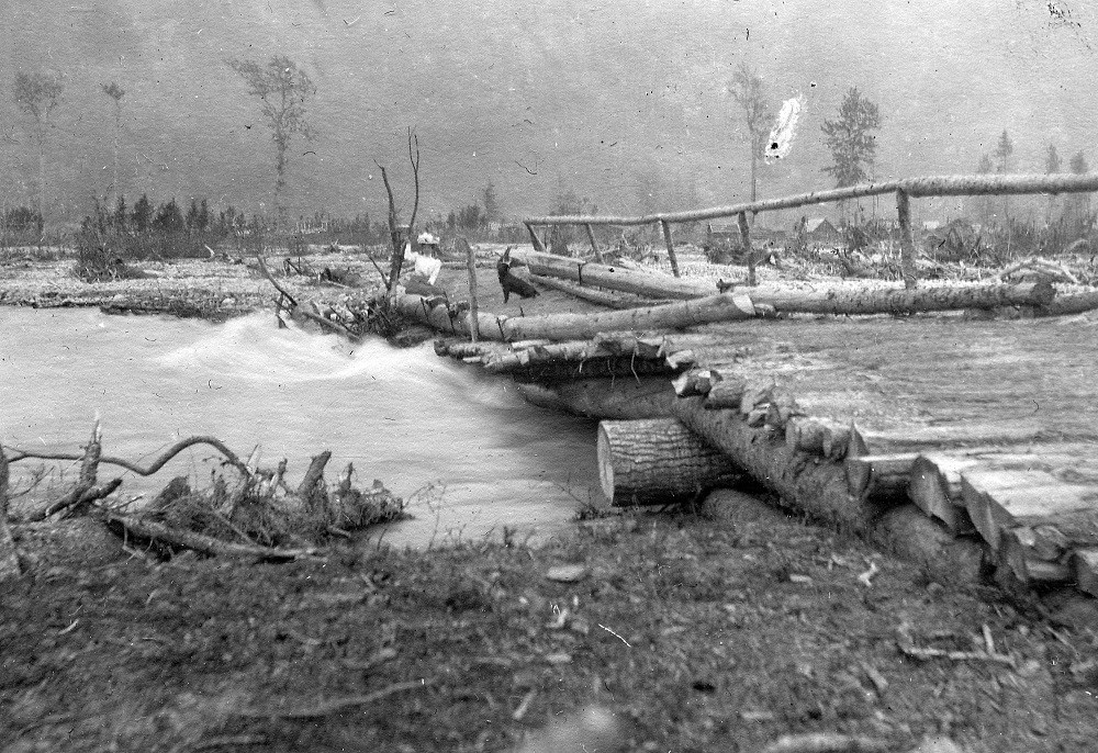 Black and white photo of a woman and dog on low bridge and rushing river