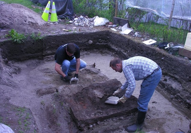 Two people working with tools in an square hole