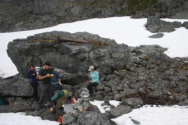 People take notes near a rusted items in a rocky and snowy area