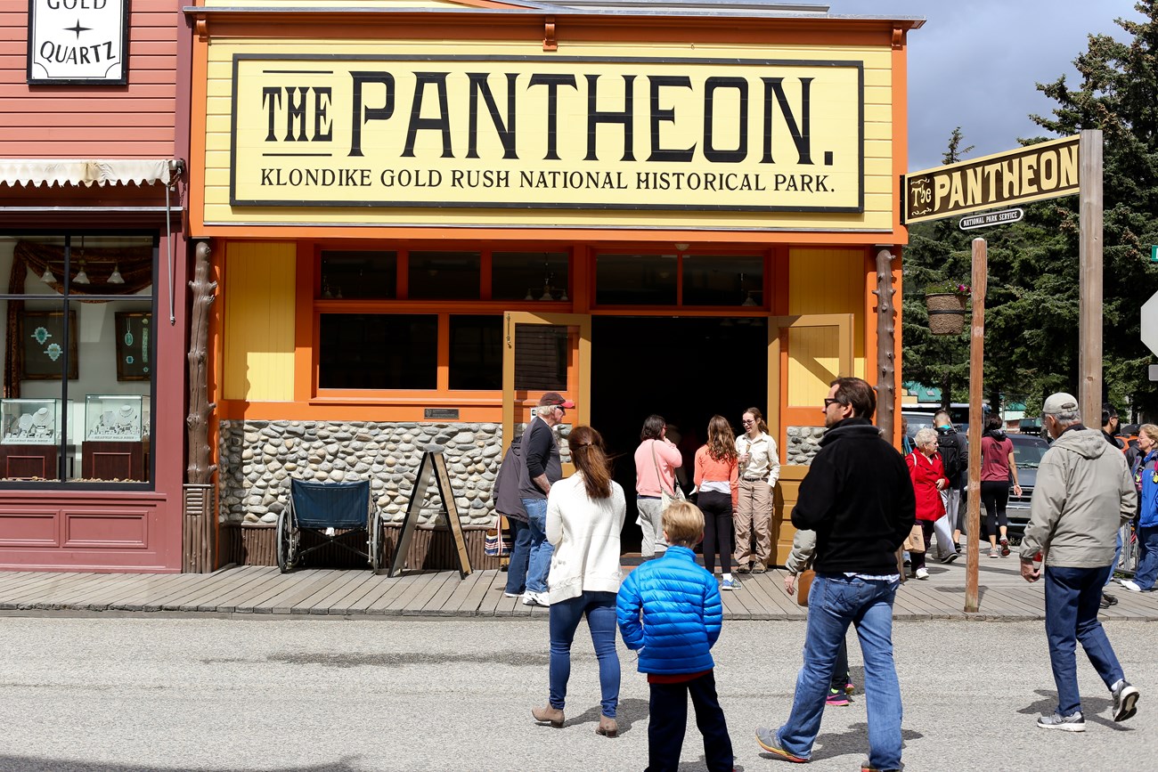 People walk in front of a brightly colored building with sign "Pantheon Saloon"