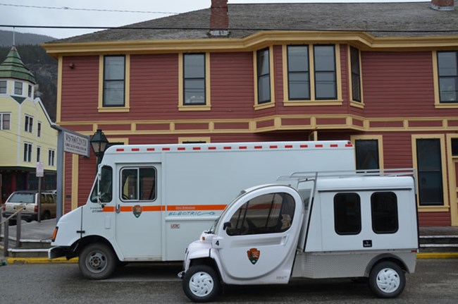 Two electric vehicles parked in front of the Visitor Center at Klondike Gold Rush National Historical Park