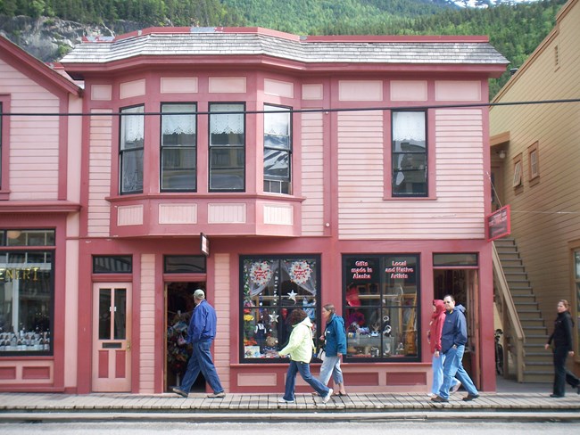 Two story pink and reddish hued Victorian style building with people walking in front Two story pink and reddish hued Victorian style building with people walking in front