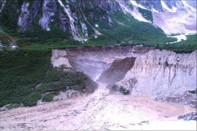 Brown water comes out of a brown wall of dirt in a natural setting.