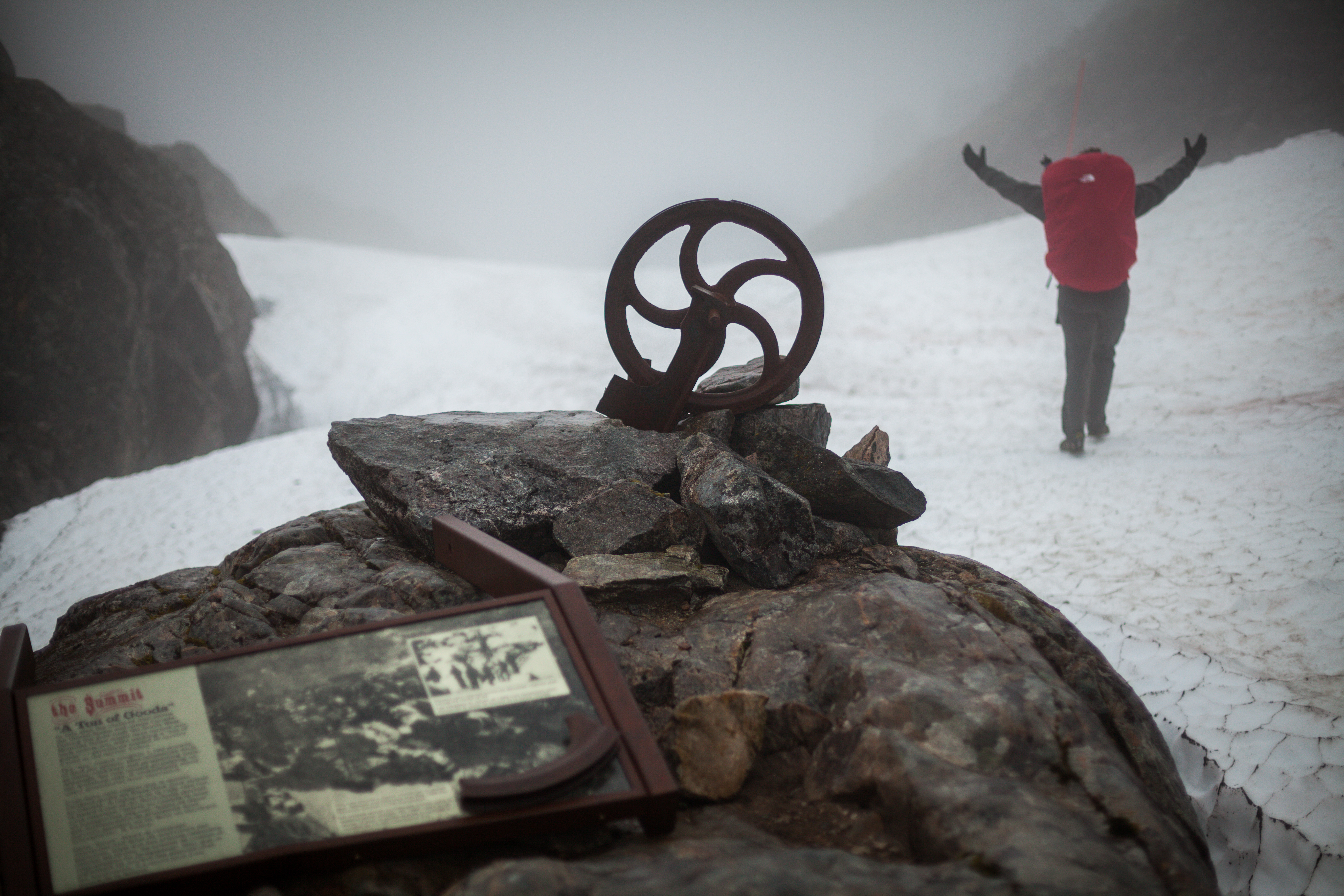 Chilkoot-34 A backpacker walks away from the camera, their arms extended in triumph as they cross over the summit of the Chilkoot pass.