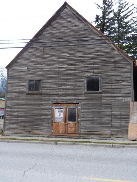 The front of the previous YMCA gym. A wooden building with two square windows and one double door.