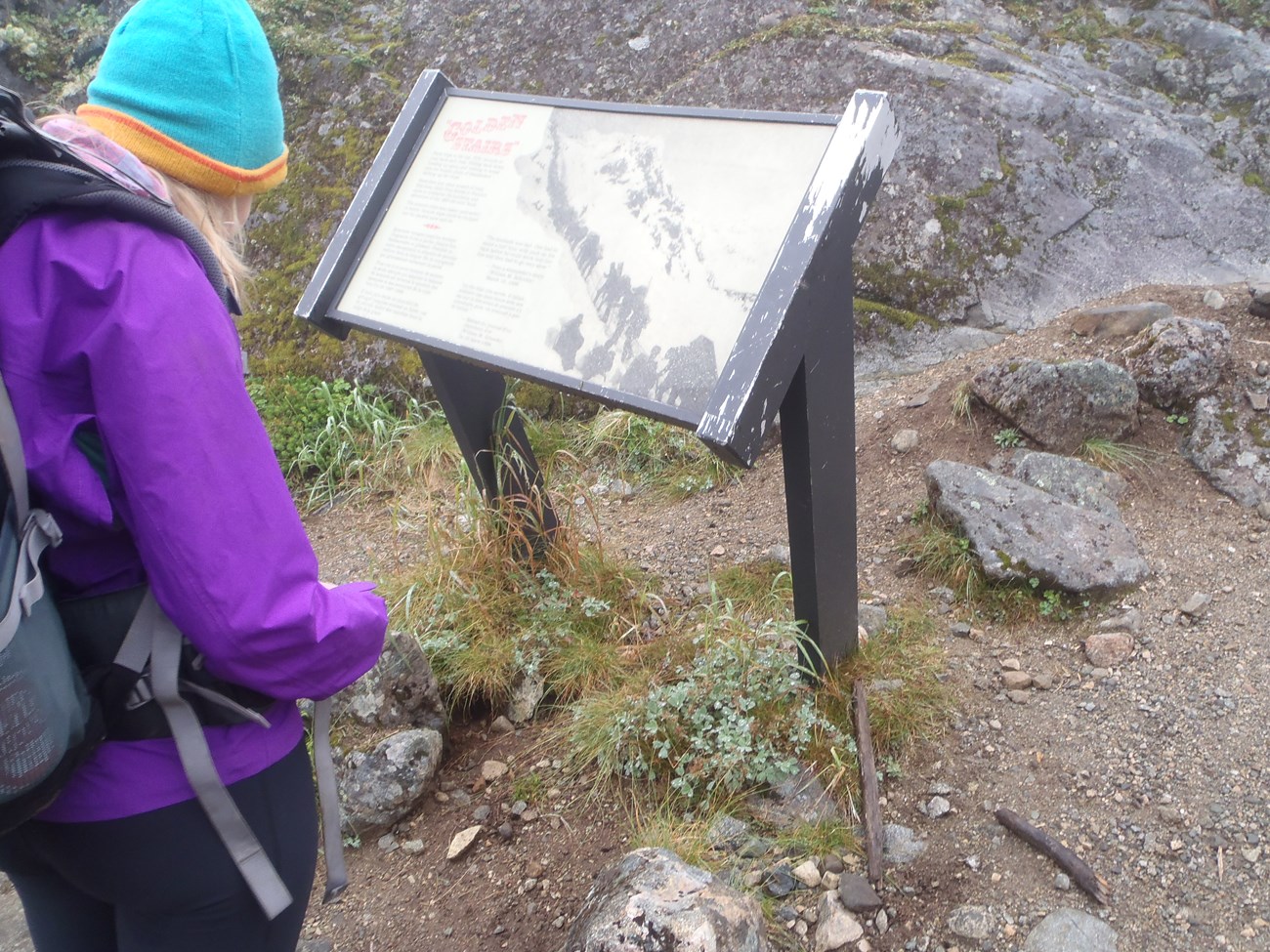 A hiker stands next to a wayside in a remote backcountry mountain pass
