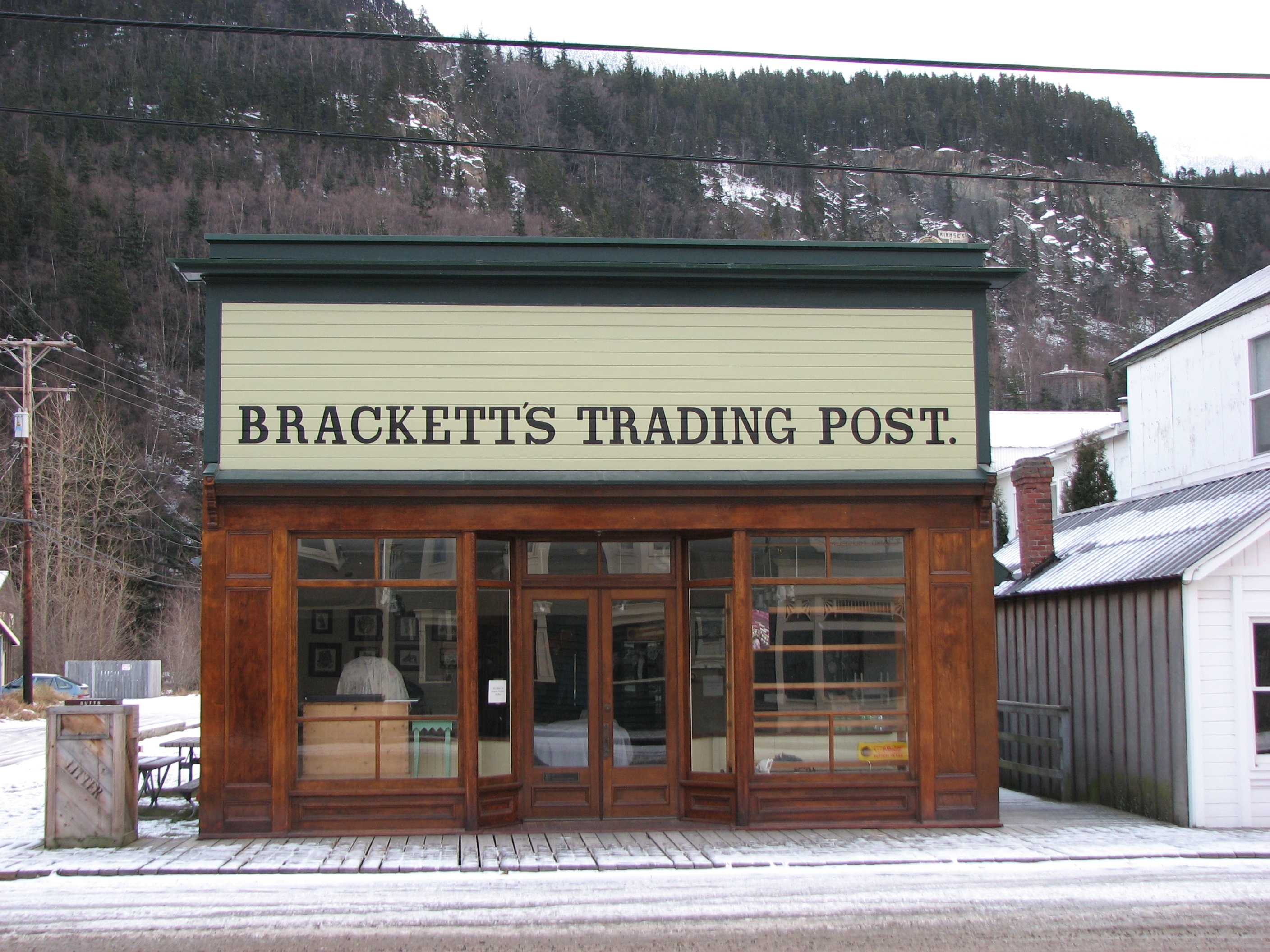wood one story building with large painted sign covering top front of entire structure. Sign says Brackett Trading Post