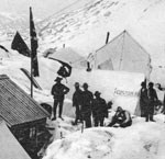 Black and white photo of people standing in snow near canvas tents.