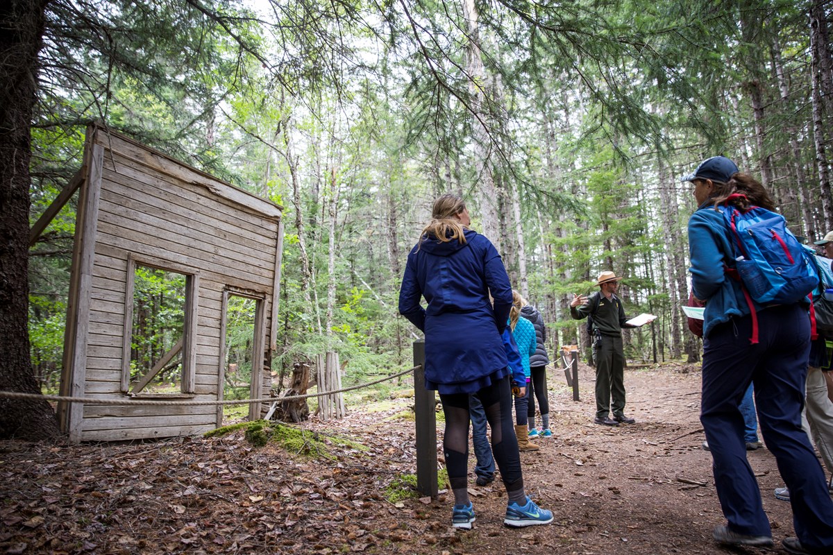 A ranger talks to people in front a false front of a building in the forest A ranger talks to people in front a false front of a building in the forest