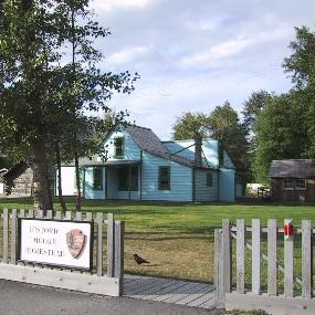 "Moore Homestead, a blue Victorian home in front of a grassy lawn.