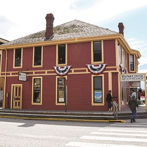 A red building with American Flags on a sunny day with a sign saying "The Visitor Center"