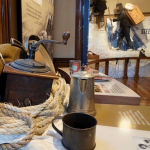 Coffee grinder, cup, and pot in the foreground.  Statues climbing in the background.