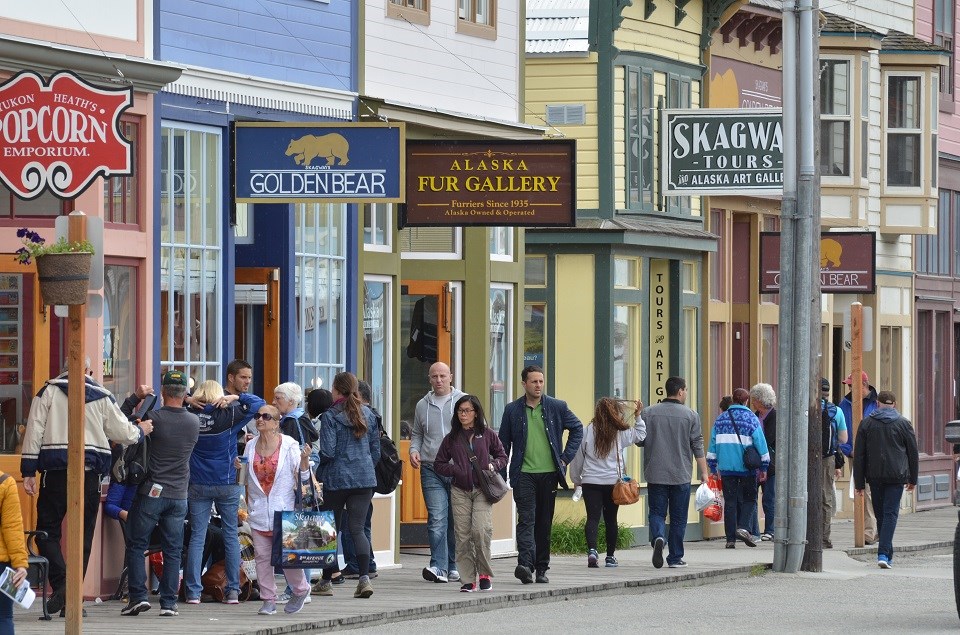 A crowd of visitors walks on wooden boardwalks in front of gold rush era buildings that are now modern stores