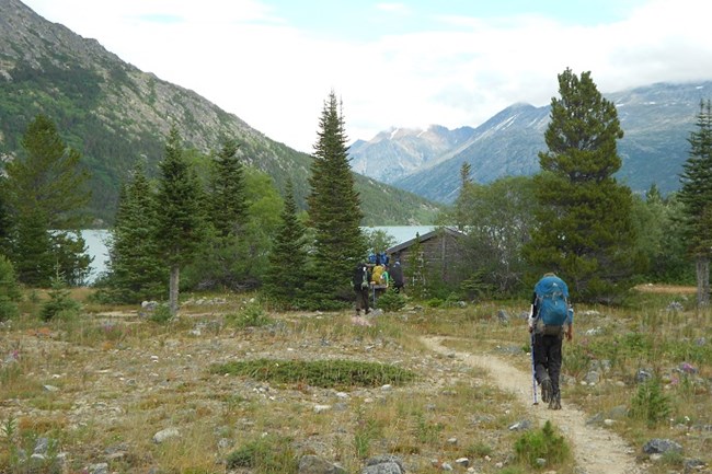 Backpapers walk toward a cabin in front of a lake