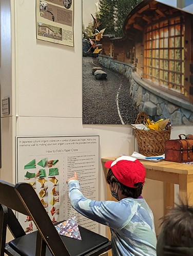 A child wearing a red hat sits on the floor pointing at a poster.