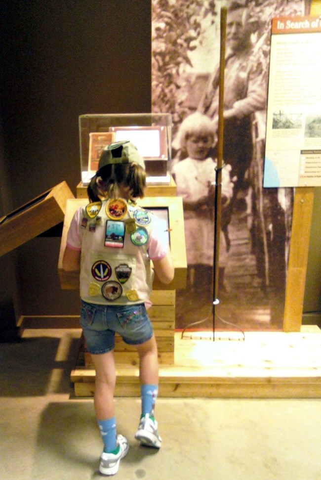 Scavenger Hunt - web version Girl hunch over a monitor wearing a vest full of patches.