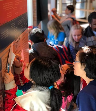 children look at exhibits and write on paper while an adult stands by