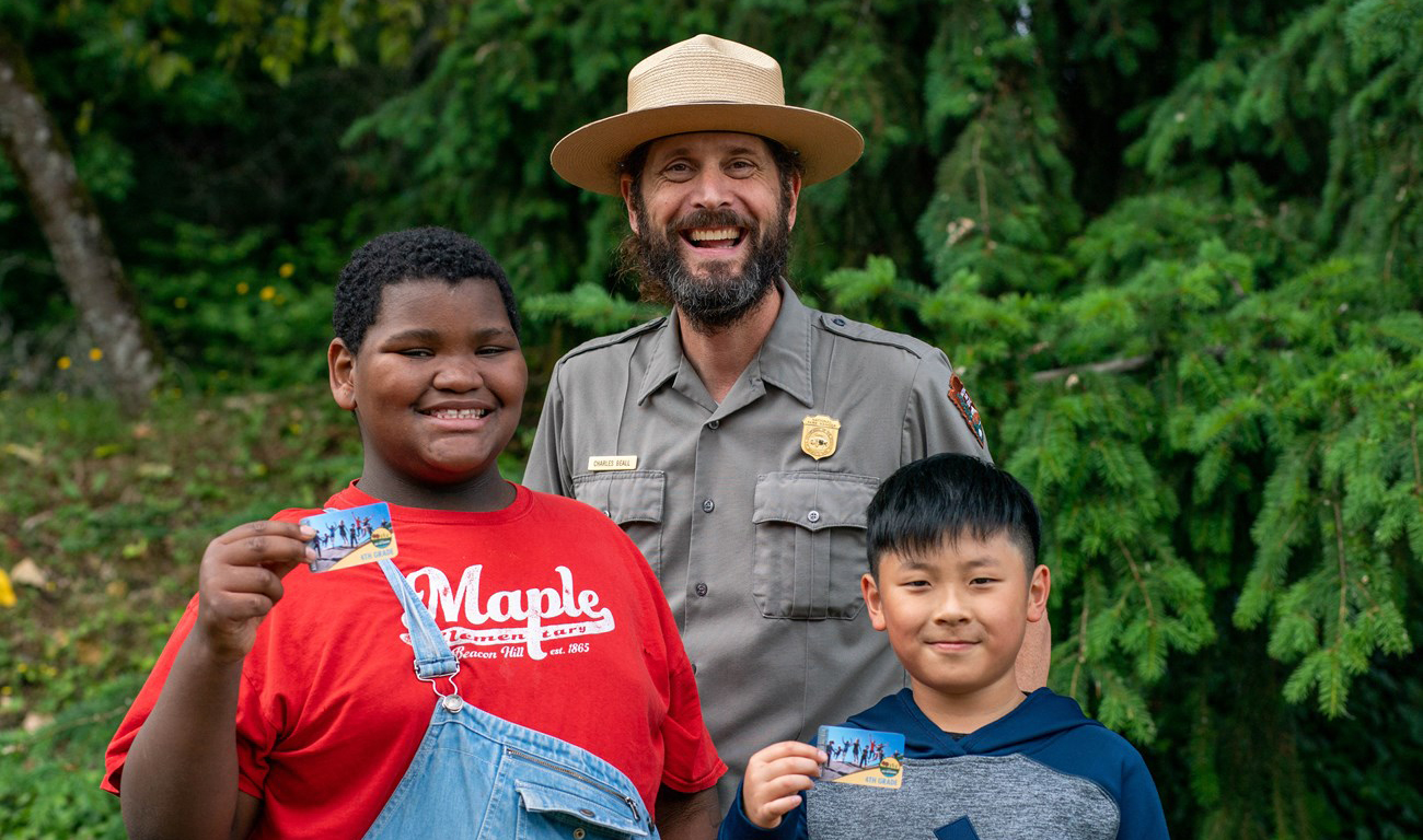 A ranger poses with two children holding up park passes.