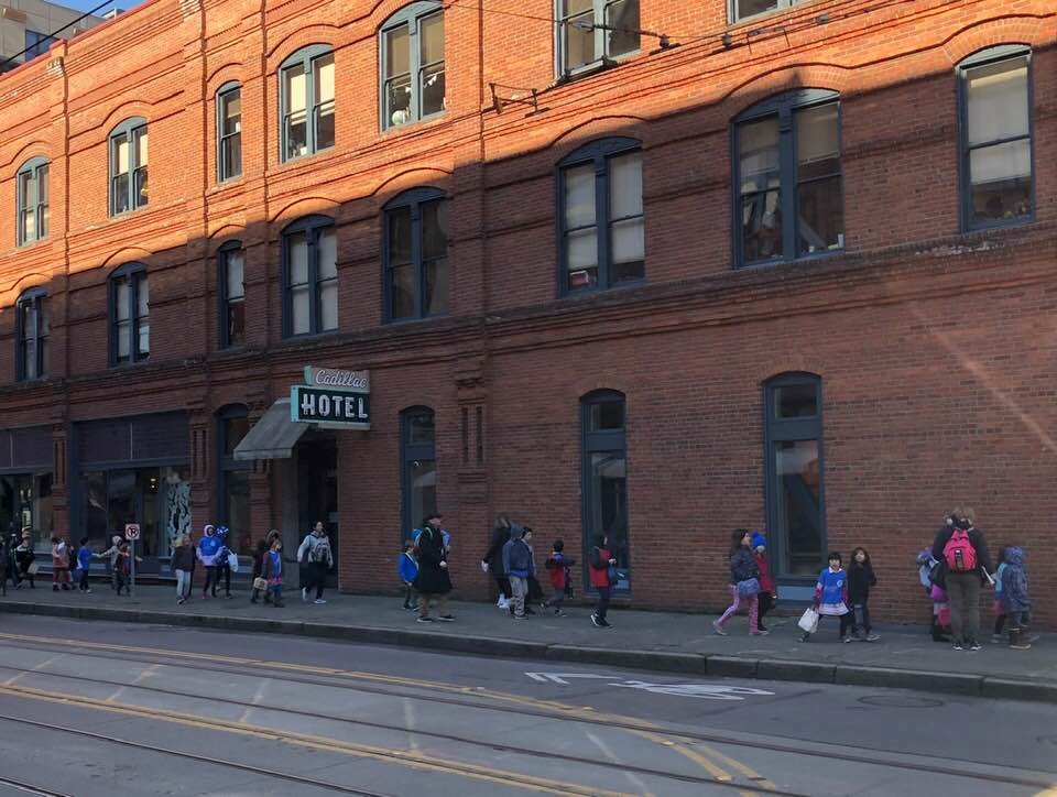 a line of kids walks along a large brick building