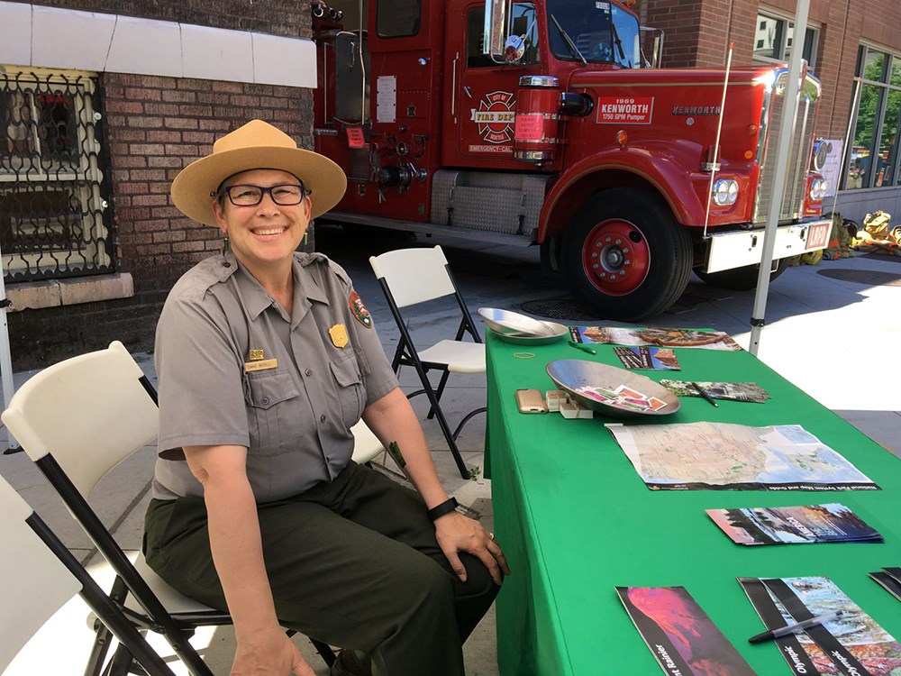 A ranger sits at a table looking at the camera.  A firetruck is in the background