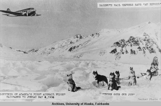 Writing Home exhibition archival photo of snow capped mountains with a dog-sled team on bottom right corner looking up at an airplane.