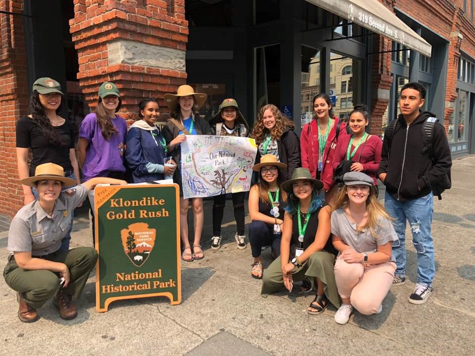 a ranger and a group of kids pose outside a building