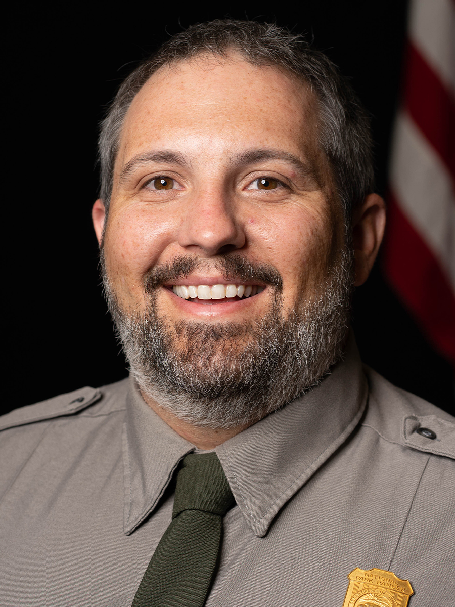 Tom Smith- Superintendent A man in a grey shirt, and green tie smiles at the camera