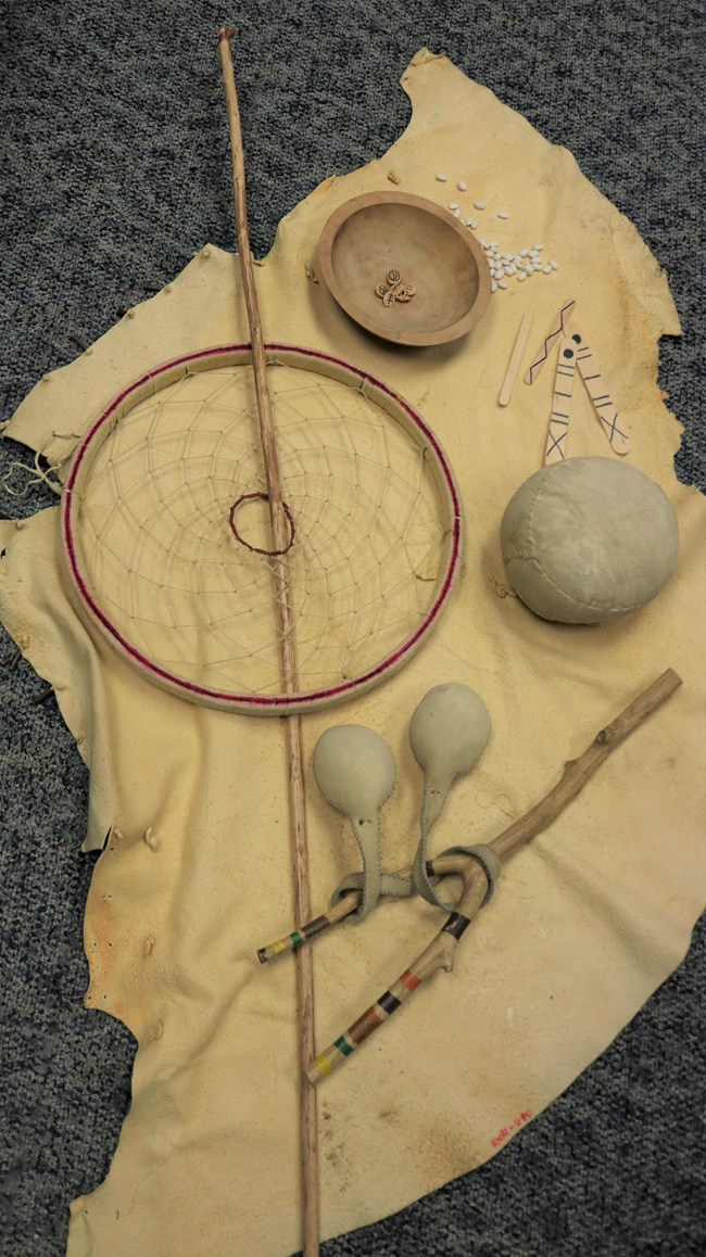 Native American game items on a piece of hide. The games are hoop and stick, double ball, hacky sack, and dish raised up.