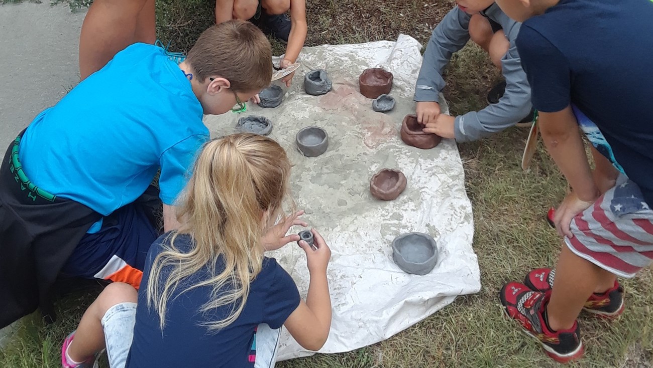 Kids gather around small clay pots.