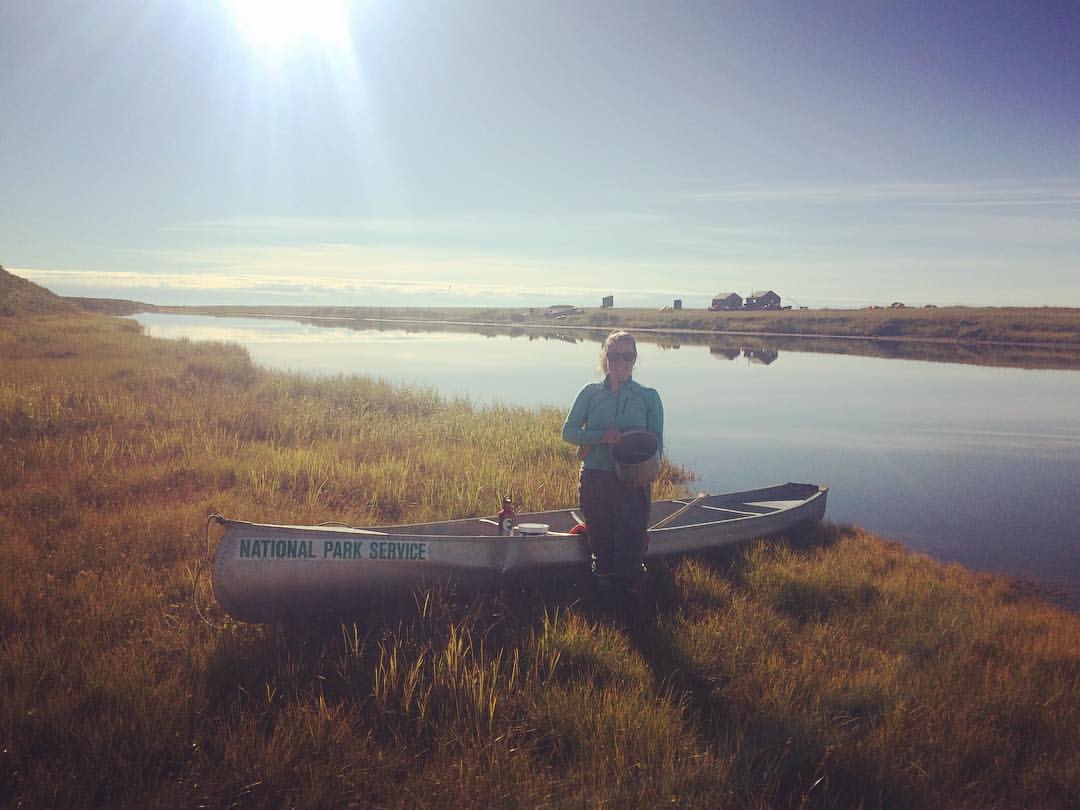Hannah stands next to a canoe and small pond holding a bucket of berries