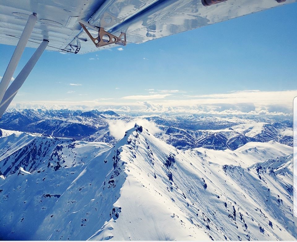 Snowy mountain peaks under a blue sky with bottom of plane wing visible at top Snowy mountain peaks under a blue sky with bottom of plane wing visible at top