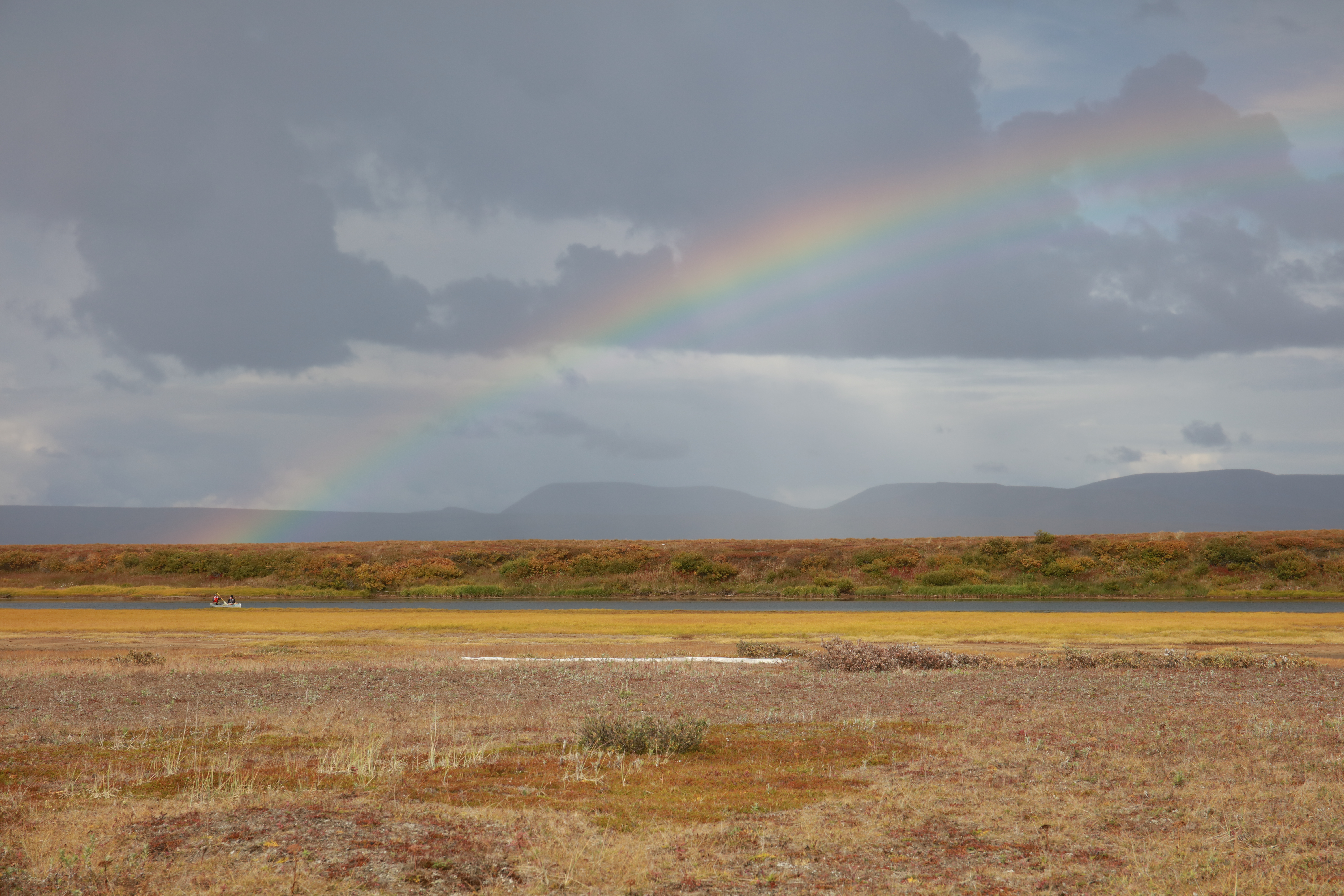 A rainbow stretched across a cloudy sky and above a yellow and green colored tundra landscape.
