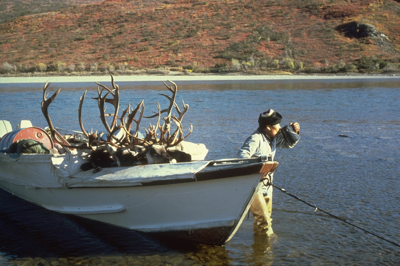 Man standing next to boat drinking a beverage after a caribou hunt.