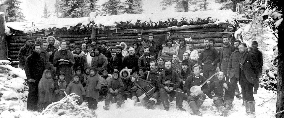 historic photo of a group of people in winter parkas in front of a snowy cabin