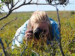 girl lying in the tundra taking a photo