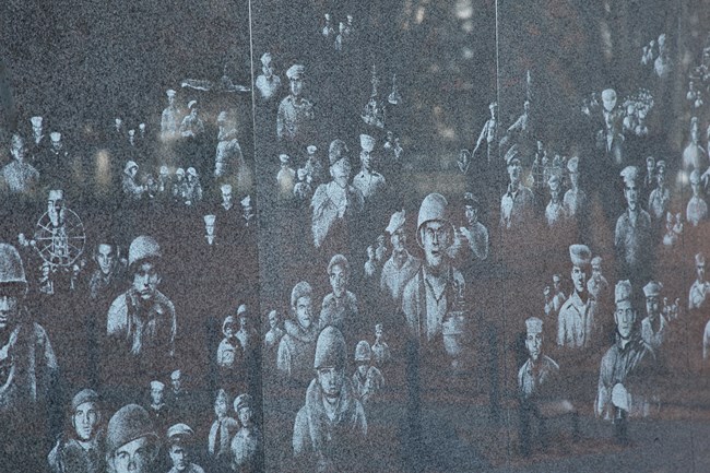 Reflective images of war veterans are displated on a stainless-steel wall.