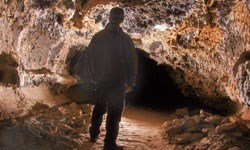 A person stands in a lava tube looking into the depths