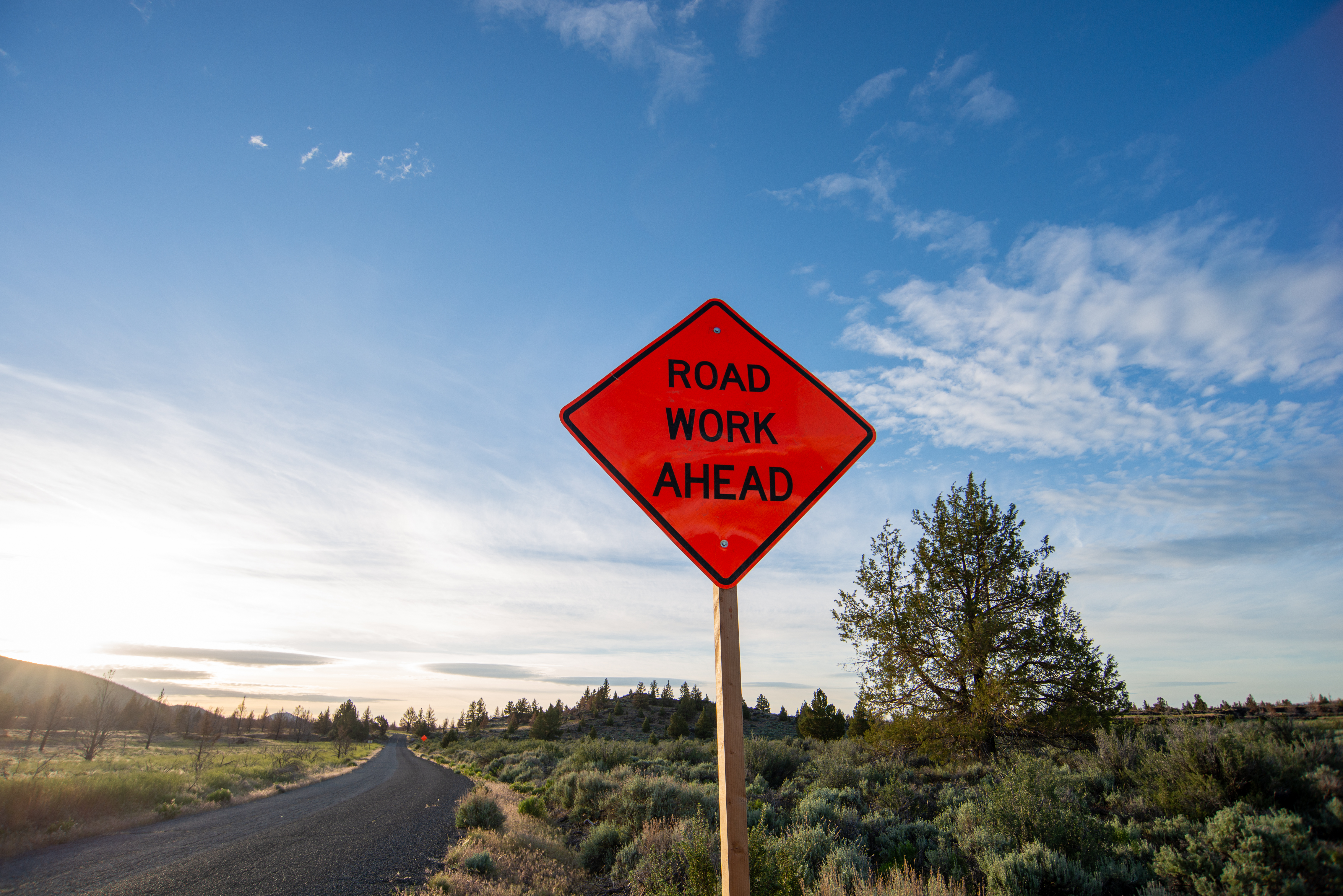 Road Work Signs-1 A orange construction sign that reads road work ahead with a blue sky in the background.