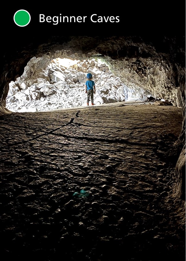 A child wearing a helmet stands in a beginner cave, with a smooth floor and relatively high ceiling.